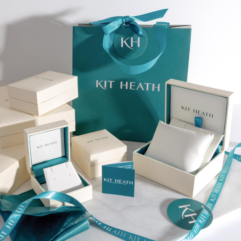 A turquoise gift bag and ivory jewelry boxes with turquoise accents sit on a white surface.