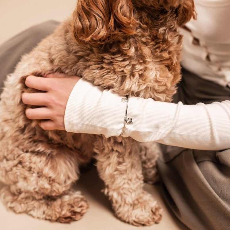 Woman in white ribbed long-sleeve shirt hugging brown dog.
