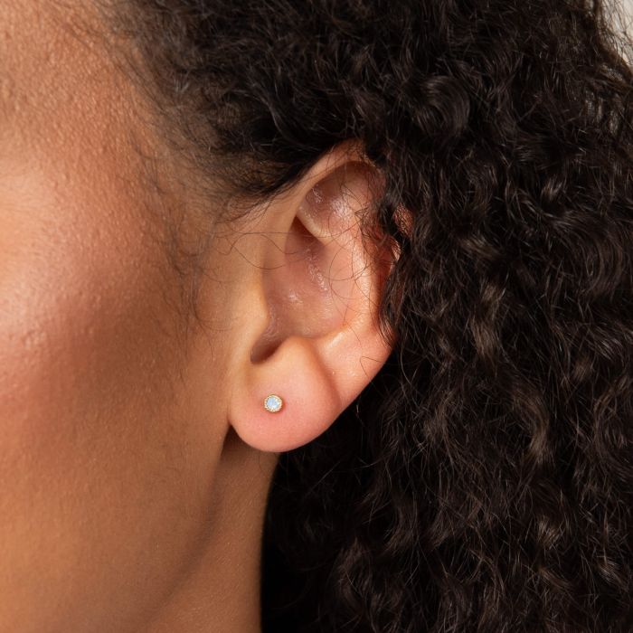 Close-up of a model's ear wearing the Laura Ashley blue crystal stud earring. Gold-plated stud earring detail.