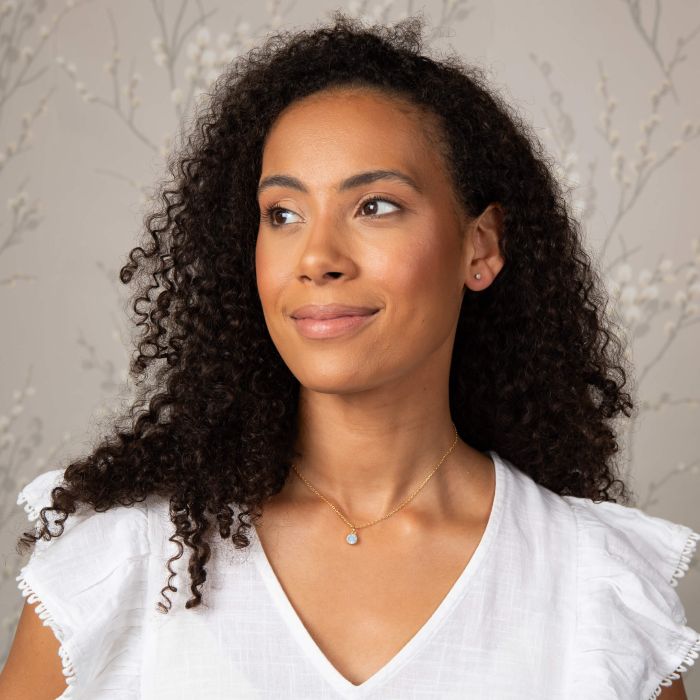 Woman wearing Laura Ashley blue crystal stud earrings and a matching pendant necklace; gold-plated jewelry set.