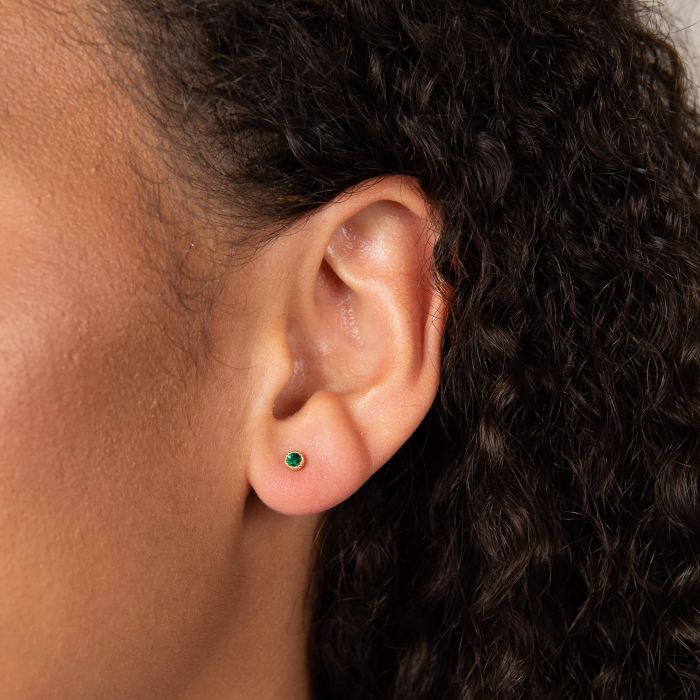 Close up of Laura Ashley gold plated stud earrings showcasing the green crystal detail on a model's ear.