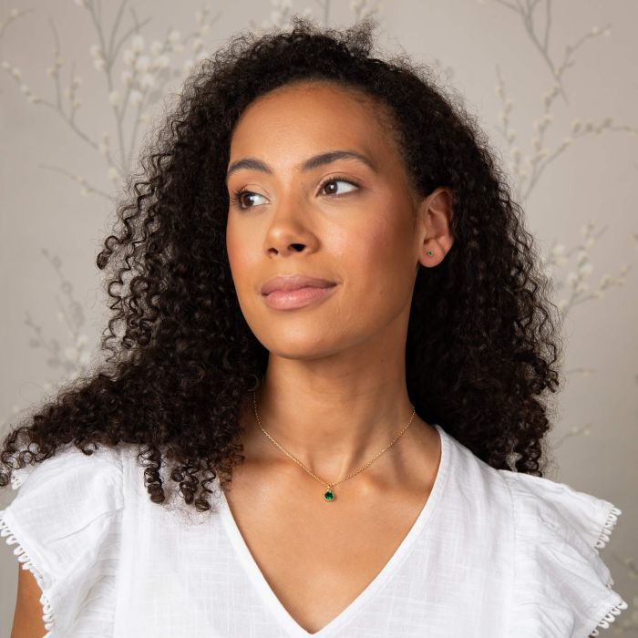 Model wears Laura Ashley gold-plated necklace and matching green crystal stud earrings. Jewelry product shot.
