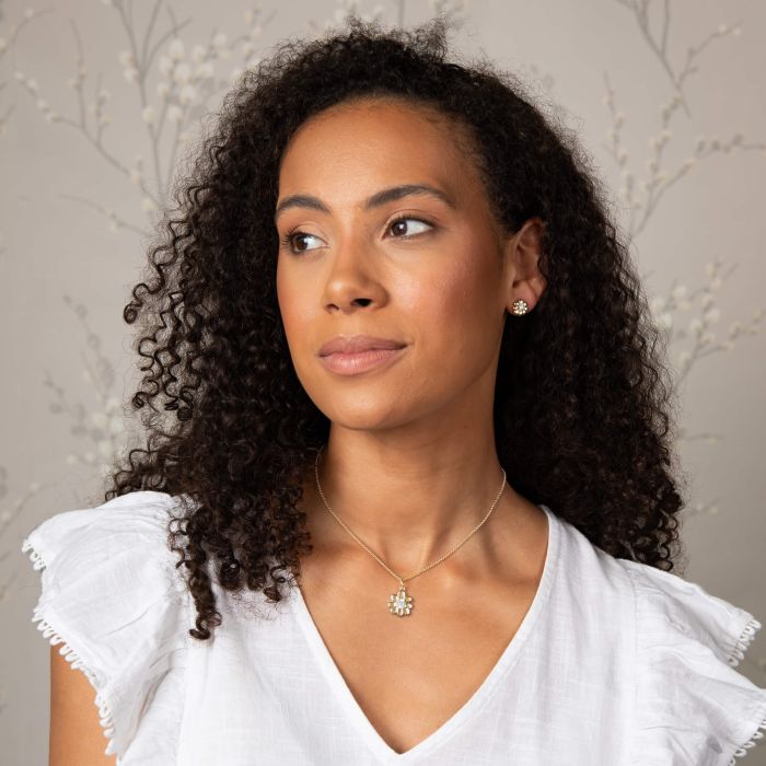 Woman wearing Laura Ashley Cosmos Flower stud earrings and necklace; gold-plated floral jewelry set.