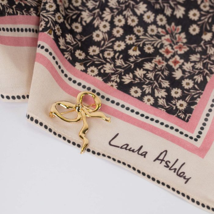 Gold plated Laura Ashley ribbon brooch pinned to a floral scarf showcasing the design and brand.